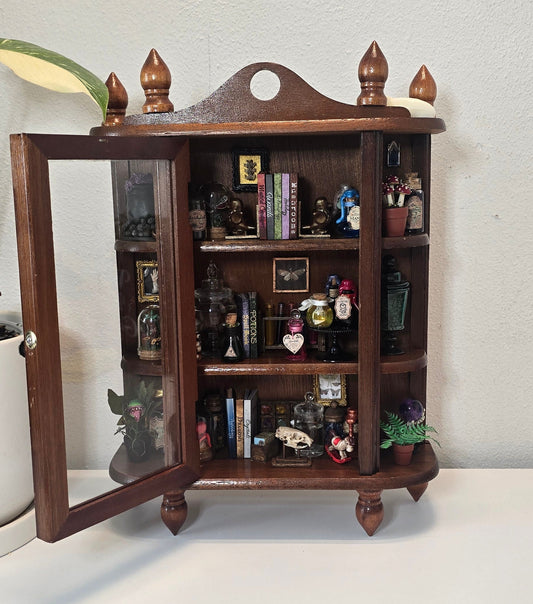 Front view of handcrafted miniature wooden curio cabinet filled with oddities, potion bottles, and skull specimens