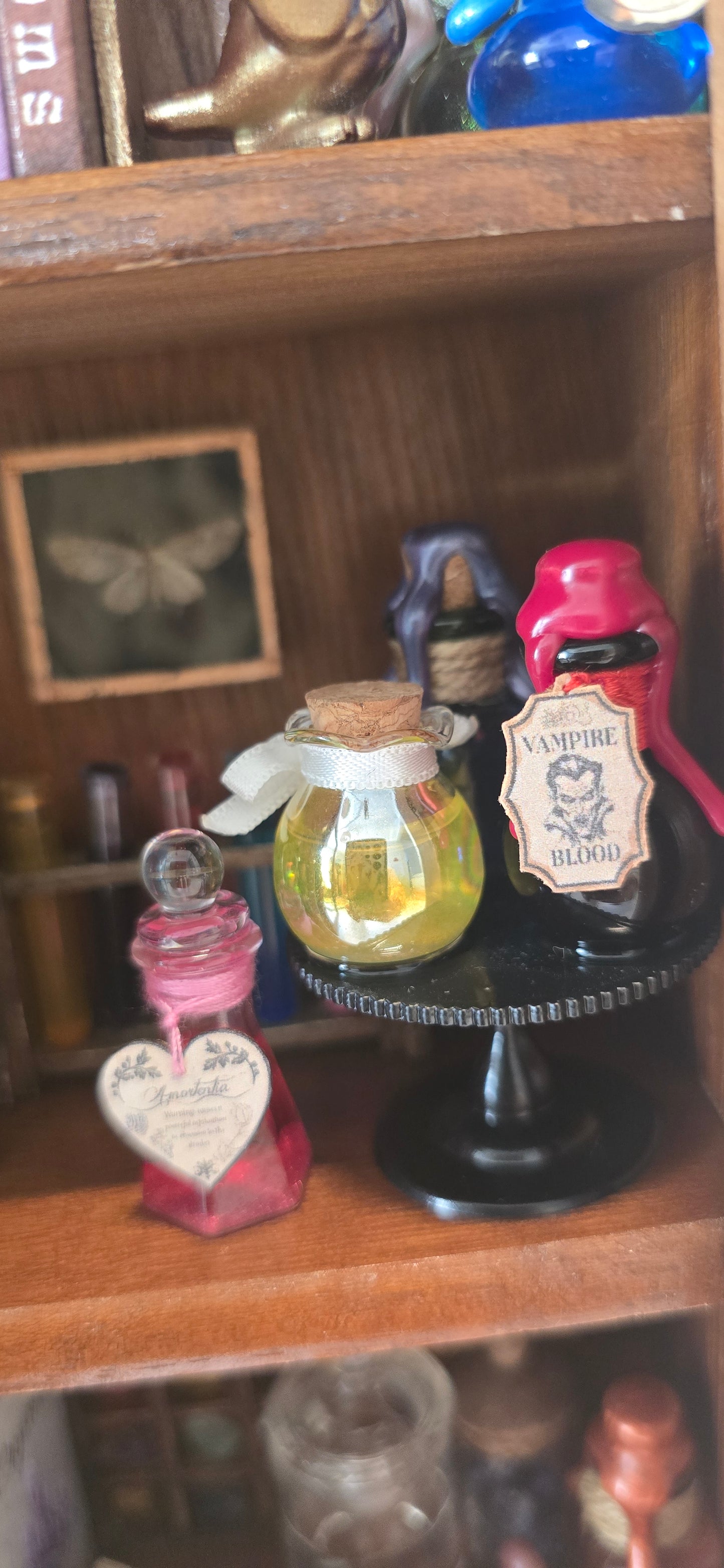 A miniature glass perfume bottle with a cork stopper and a small heart-shaped tag, displayed inside a wooden drawer alongside other small decorative items.